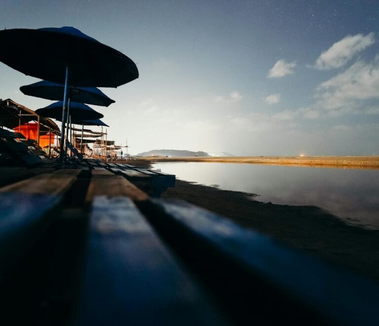 A tranquil beach view at twilight with rows of beach umbrellas and a serene ocean backdrop.