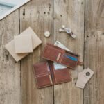 Brown leather wallet with cash, cards, and a watch on a rustic wooden background.