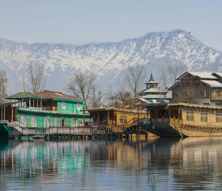 green and brown wooden house on lake near snow covered mountain during daytime