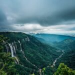 a lush green valley with a waterfall in the distance