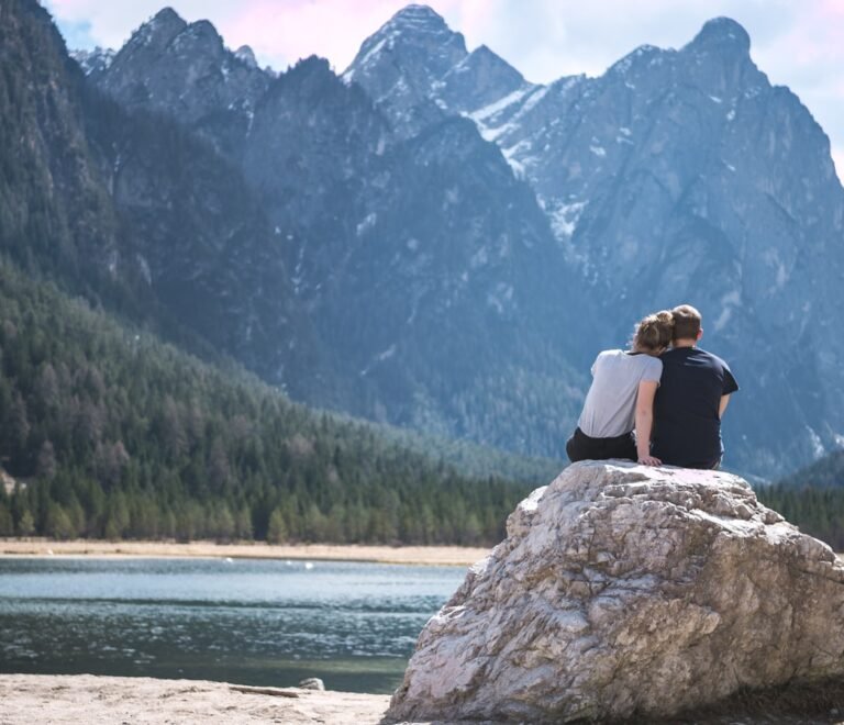 a couple sits on a rock looking out over a lake