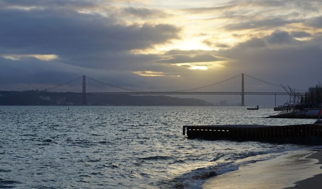 the sun is setting over the water and a bridge is in the distance